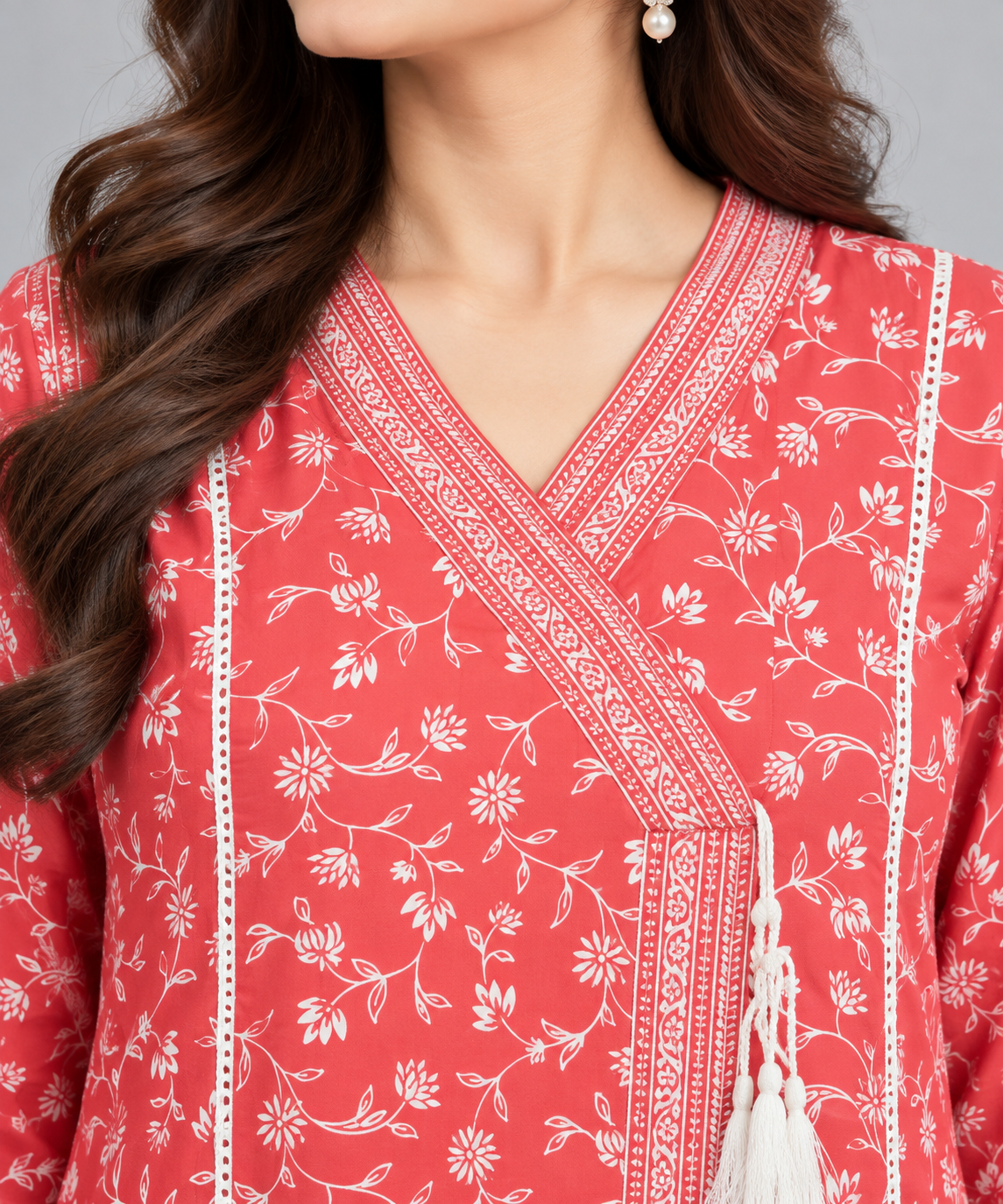 Close-up of a coral pink printed women's kurta featuring white floral patterns, detailed V-neck border and decorative tassel accents.