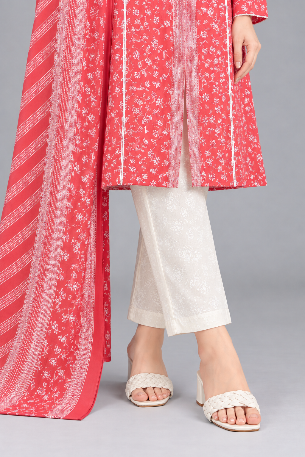 Close-up of a coral pink printed kurta with white floral pattern, matching printed dupatta and white straight trousers.