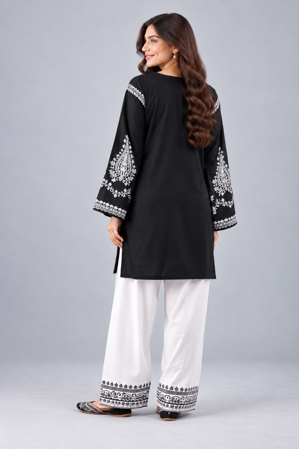 Back view of black kurta with embroidered sleeves and white trousers.